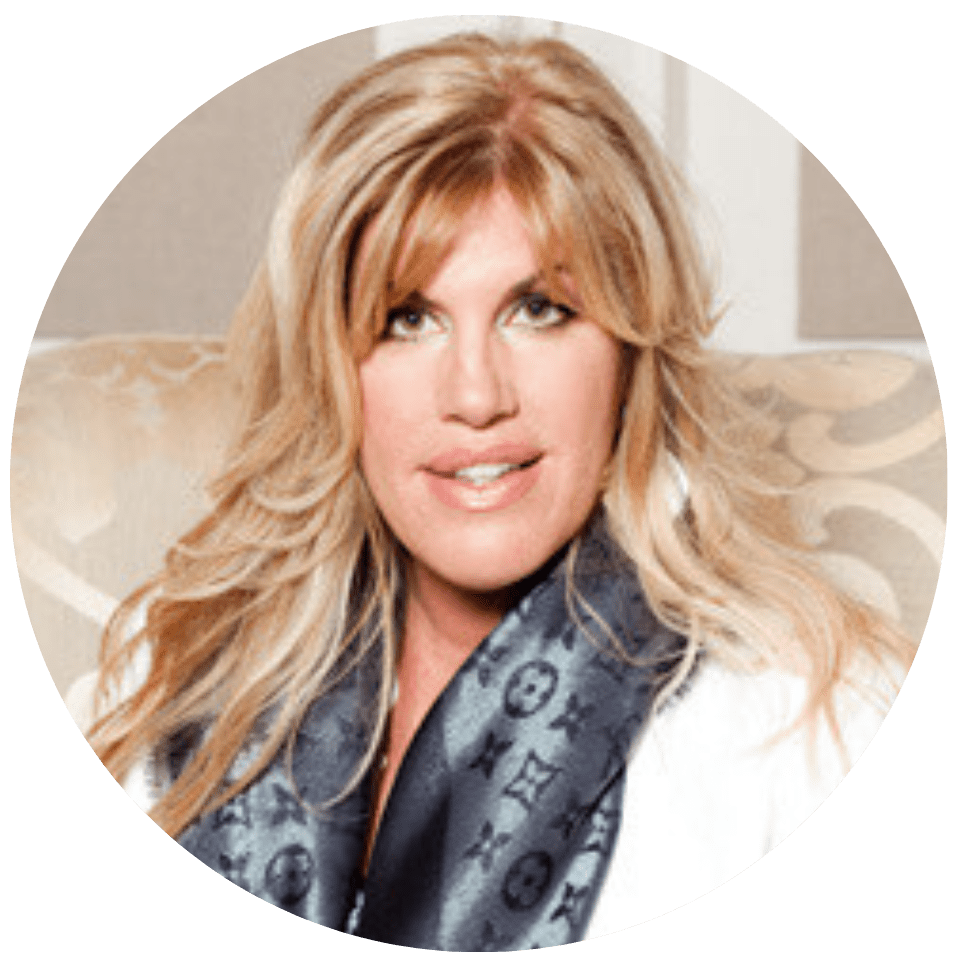 A woman with long blonde hair smiling, wearing a black jacket, and resting her chin on her hand. The background features abstract blue and white artwork and a green plant.